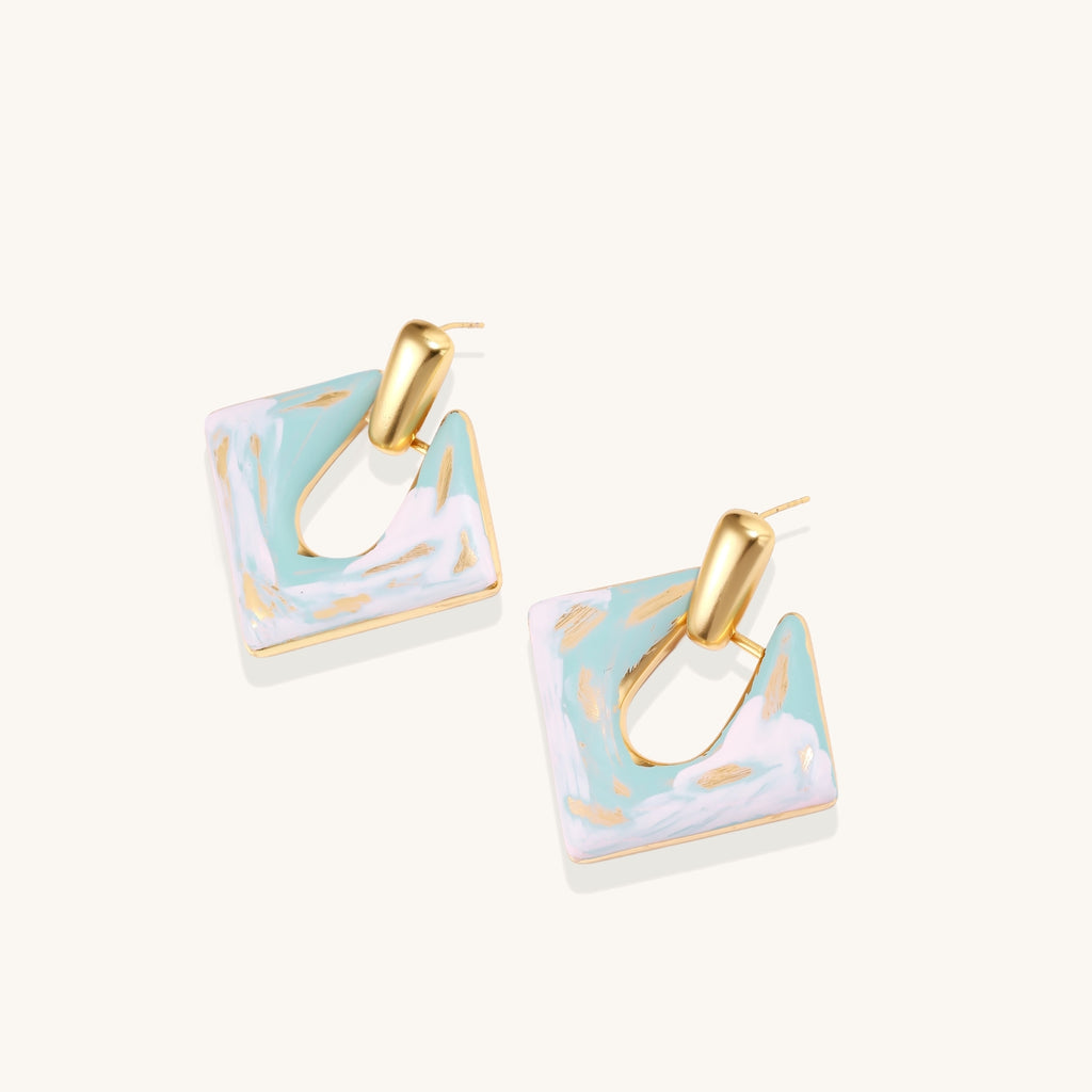 Diamond-shaped gold-plated earrings with pastel marble enamel in turquoise and lavender swirls on beige background