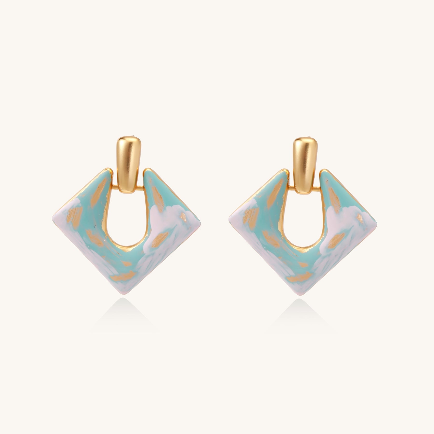 Diamond-shaped gold-plated earrings with pastel marble enamel in turquoise and lavender swirls on beige background