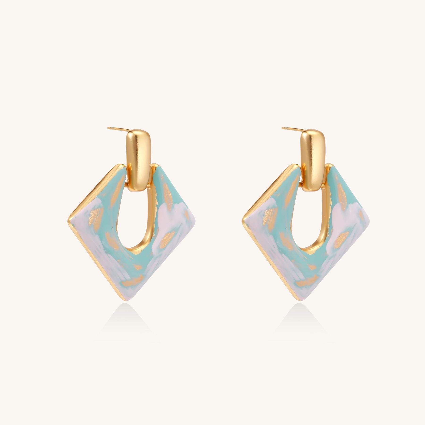 Diamond-shaped gold-plated earrings with pastel marble enamel in turquoise and lavender swirls on beige background
