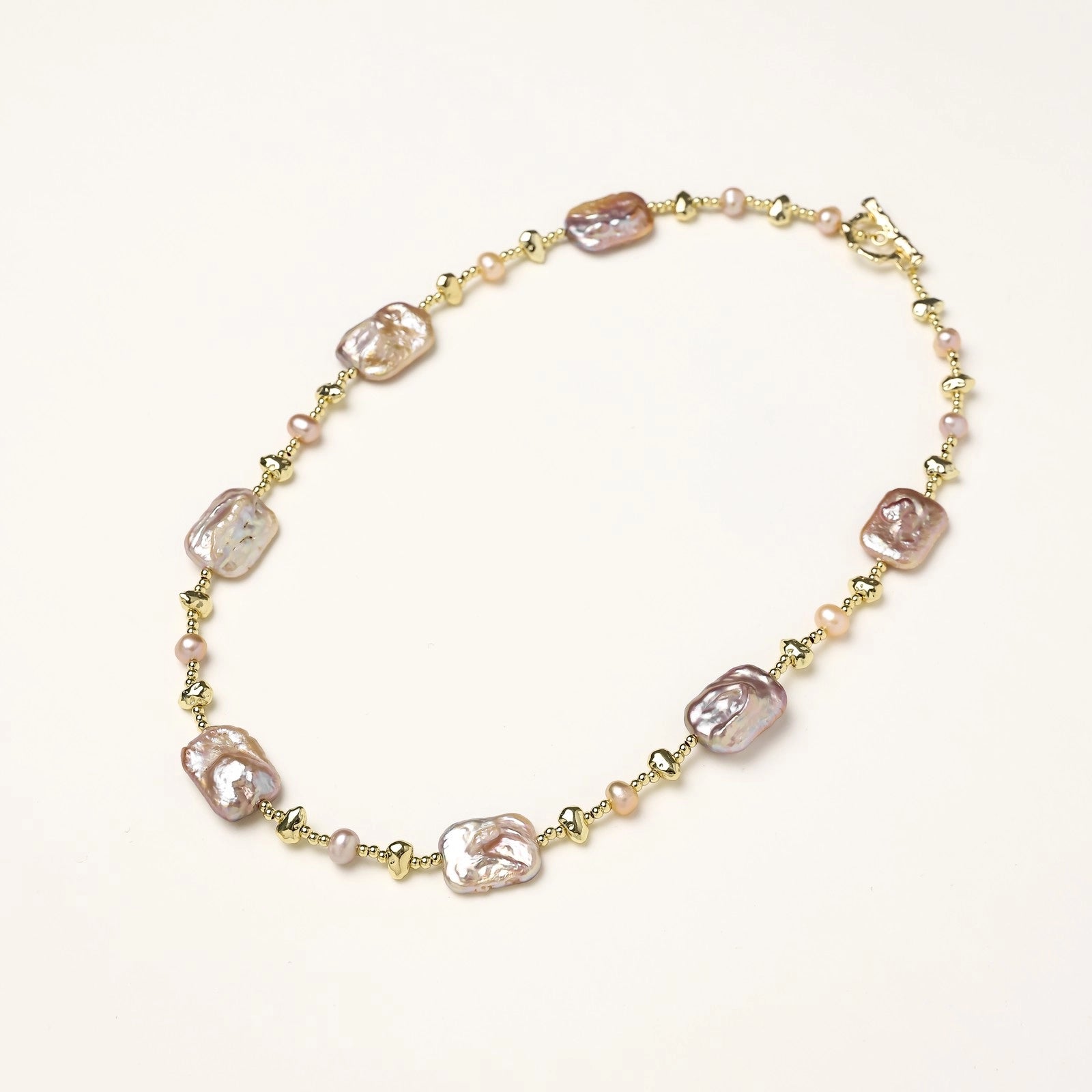 Long gold-plated necklace with iridescent baroque pearls and round freshwater pearls on cream background