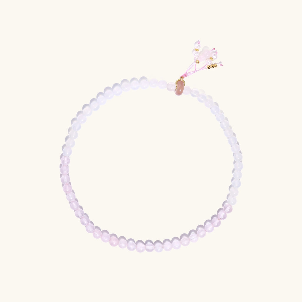 Stretchable bracelet with pink rose quartz and white agate beads, featuring a decorative tassel pendant on white background.