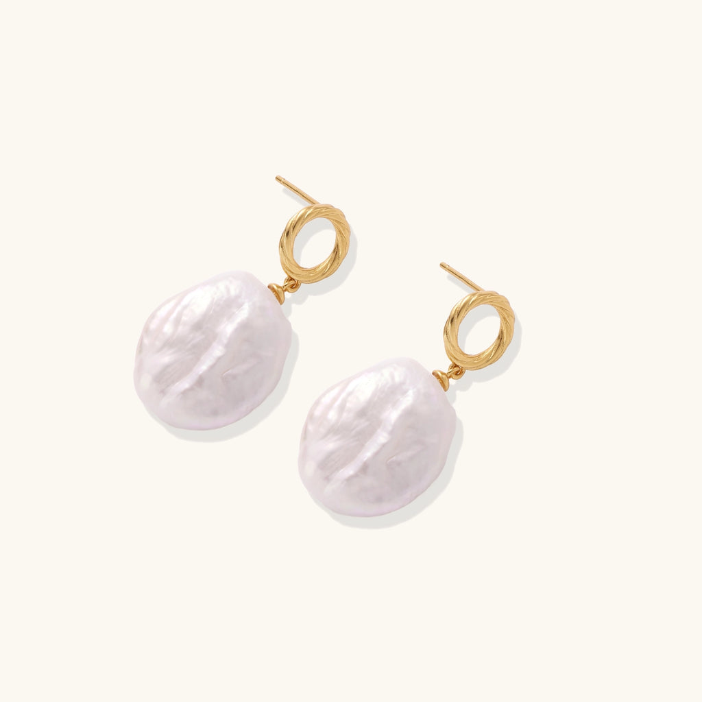 Gold-plated twisted stud earrings with large blush baroque pearls hanging elegantly on white background.