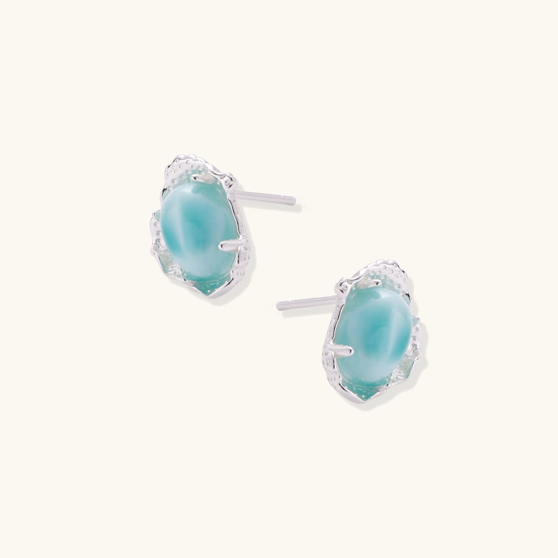 Close-up of sterling silver stud earrings with oval larimar stones in flowing wave-like settings on white background.
