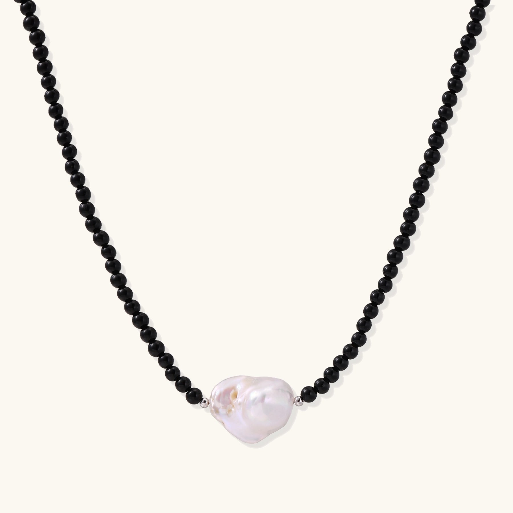 Elegant necklace with black agate beads and iridescent baroque freshwater pearl centerpiece on white background.