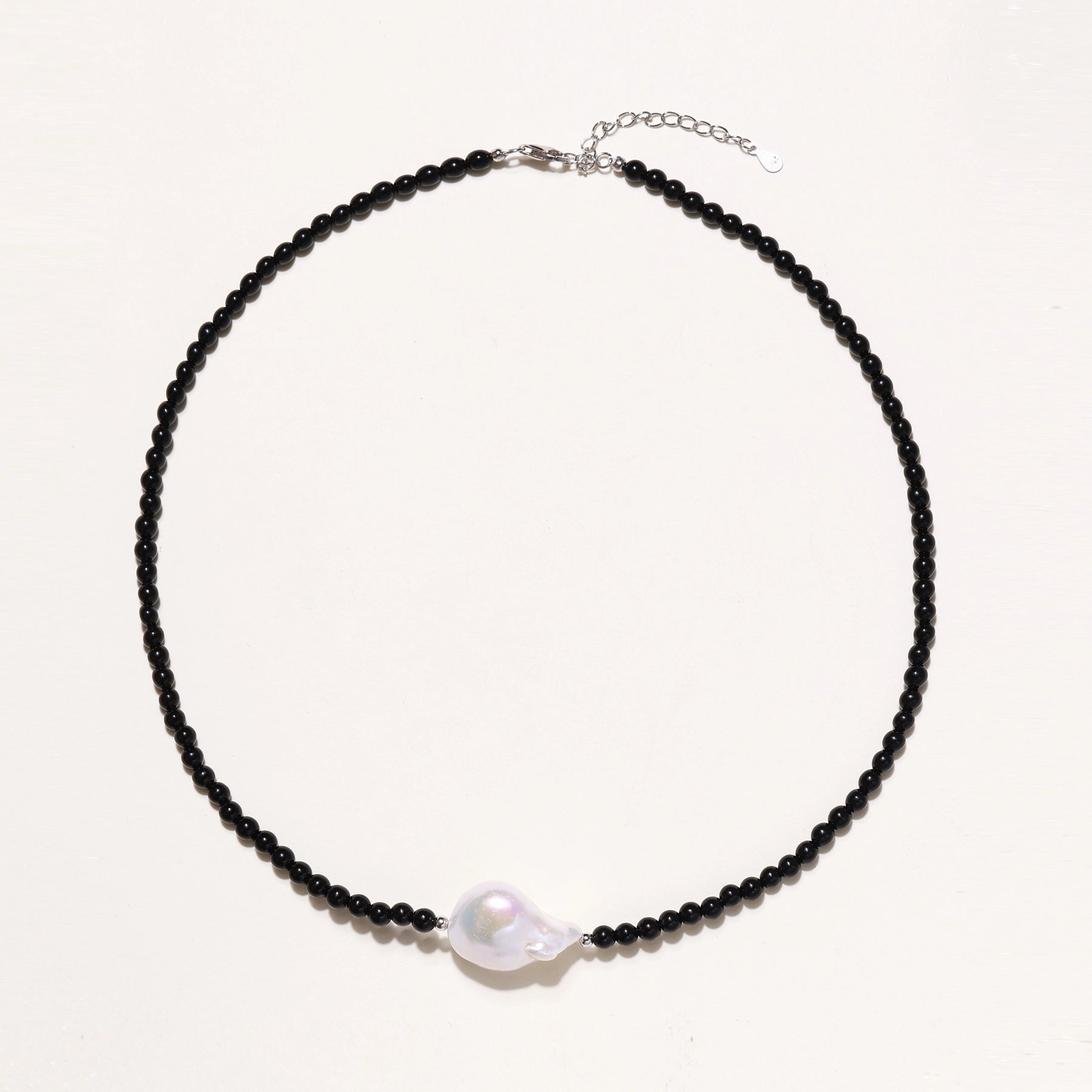 Elegant necklace with black agate beads and iridescent baroque freshwater pearl centerpiece on white background.