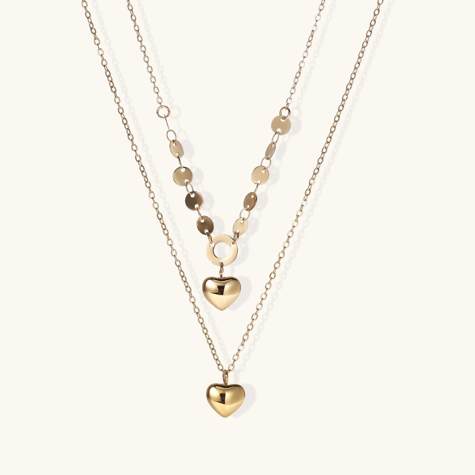 Three-layer 14K gold plated necklace with coin discs and dual heart pendants on cream background